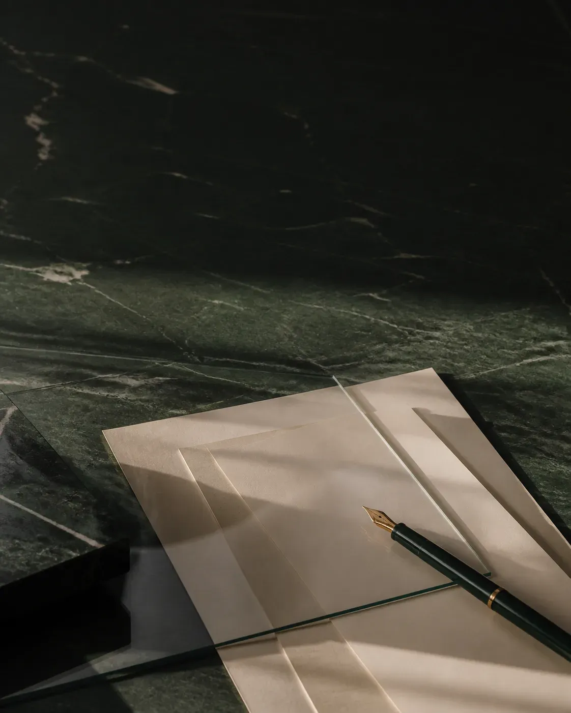 Documents crème et stylo sur une table en pierre vert profond, évocation de la coordination juridique internationale